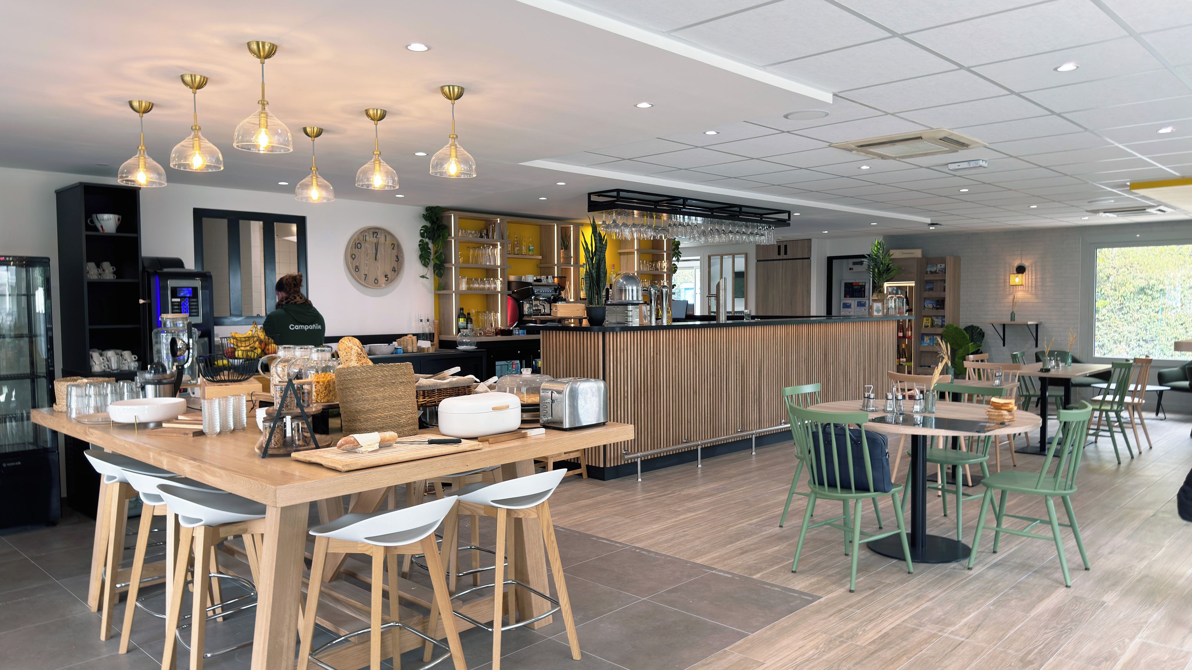 Un café moderne avec un bar, des tables en bois et des chaises vertes.