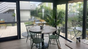 A modern interior with a dining area featuring round tables and chairs, large windows offering a view of the outdoor patio, and a ceiling with recessed lighting. - Campanile Chambray Les Tours (Chambray-les-Tours)