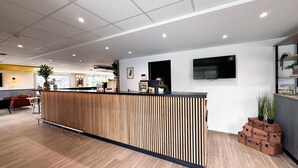 A reception desk with a wooden slat design, a flat-screen TV mounted on the wall, and a potted plant on the right. - Campanile Chambray Les Tours (Chambray-les-Tours)