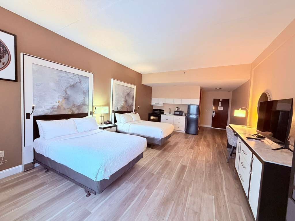 Una habitación de hotel con dos camas, una kitchenette, un televisor y obras de arte en las paredes.