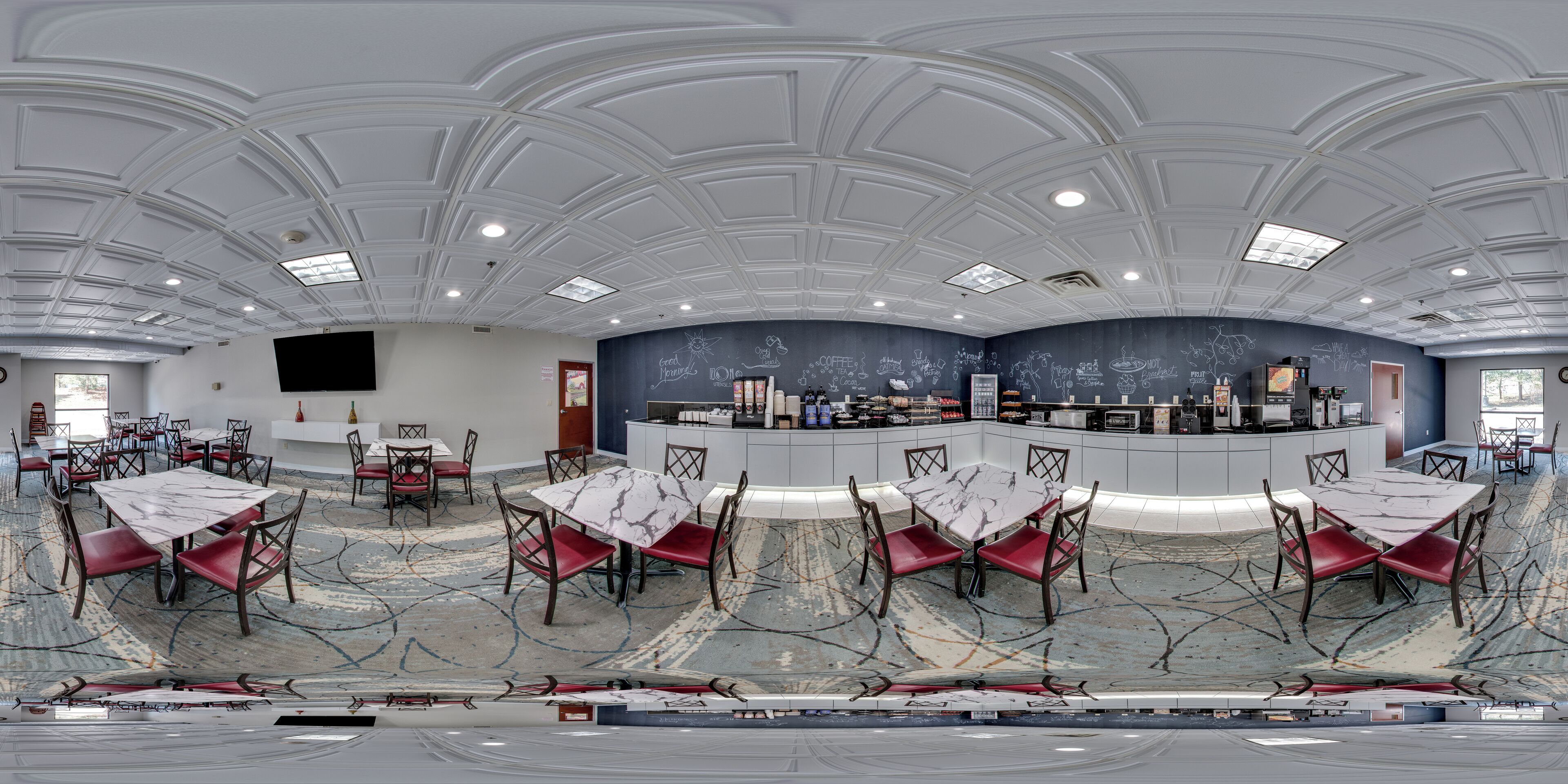 Une pièce spacieuse avec un plafond haut, de nombreuses tables et chaises, un comptoir central où sont exposés divers objets, et une grande fenêtre qui laisse entrer la lumière naturelle.