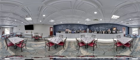 Une pièce spacieuse avec un plafond haut, de nombreuses tables et chaises, un comptoir central où sont exposés divers objets, et une grande fenêtre qui laisse entrer la lumière naturelle.
