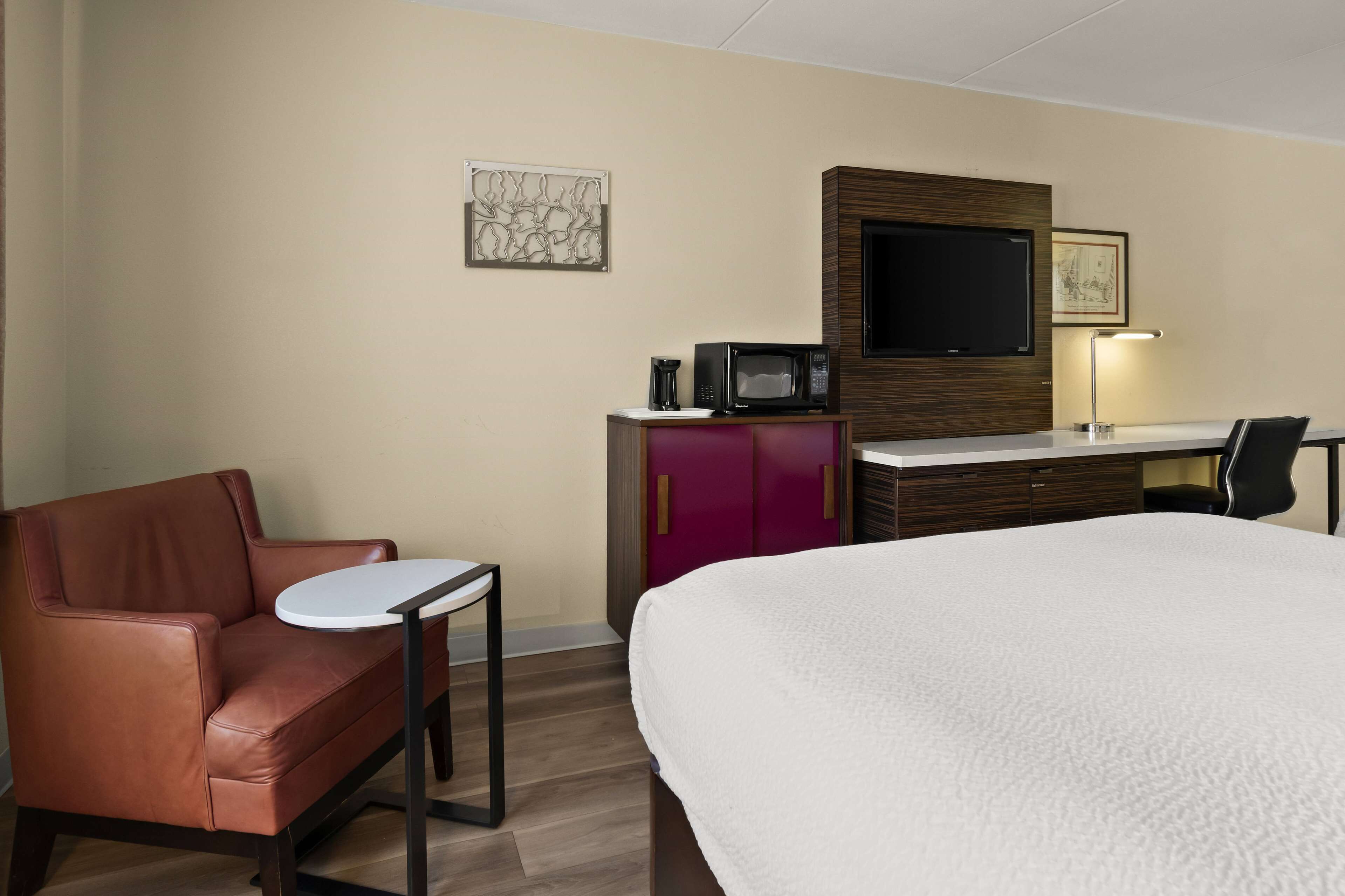 A hotel room with a bed, a desk with a computer, a chair, a small table, and a television.