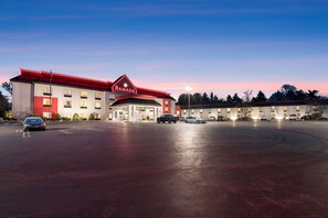 Un hôtel à la façade rouge et blanche, doté de nombreux espaces de stationnement et d’un grand parking.