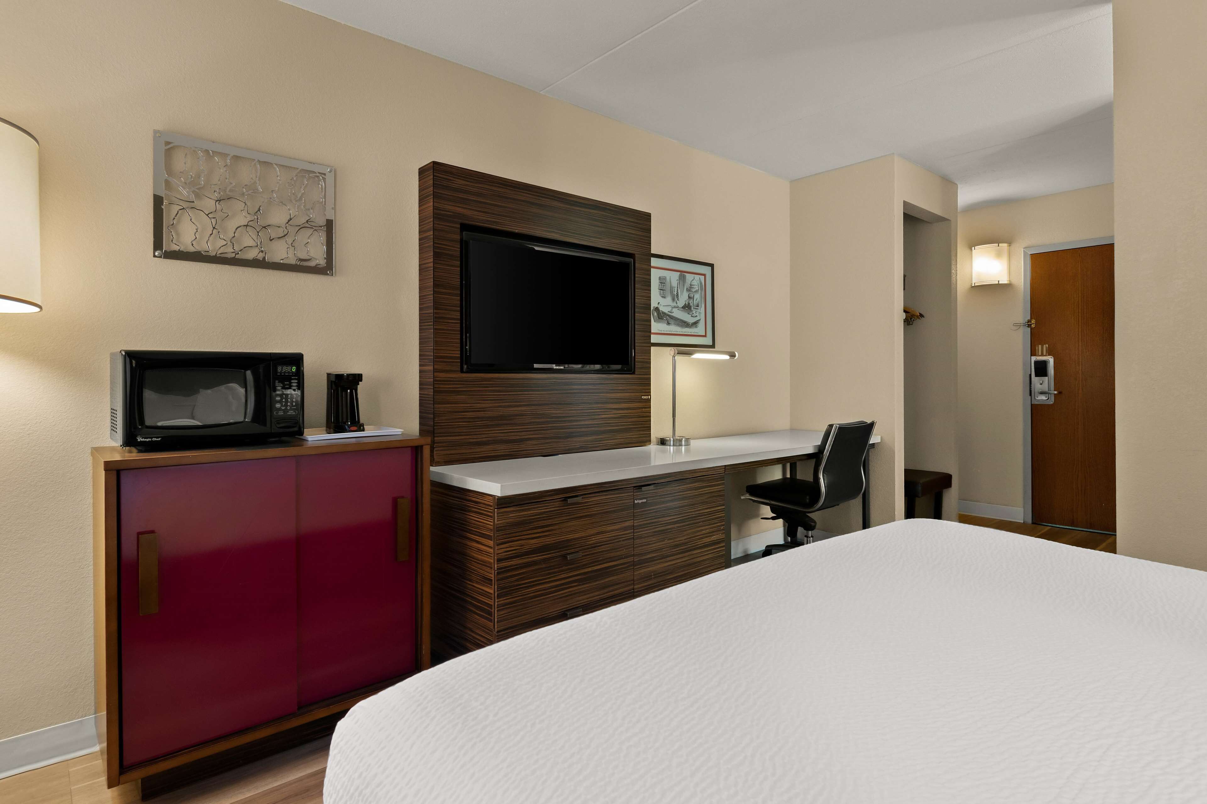 A hotel room with a bed, a desk, a TV, a microwave, and a cabinet.