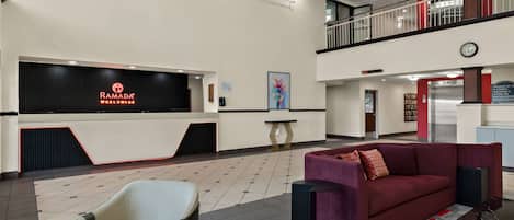 A modern hotel lobby with a reception desk, seating area, and a staircase.
