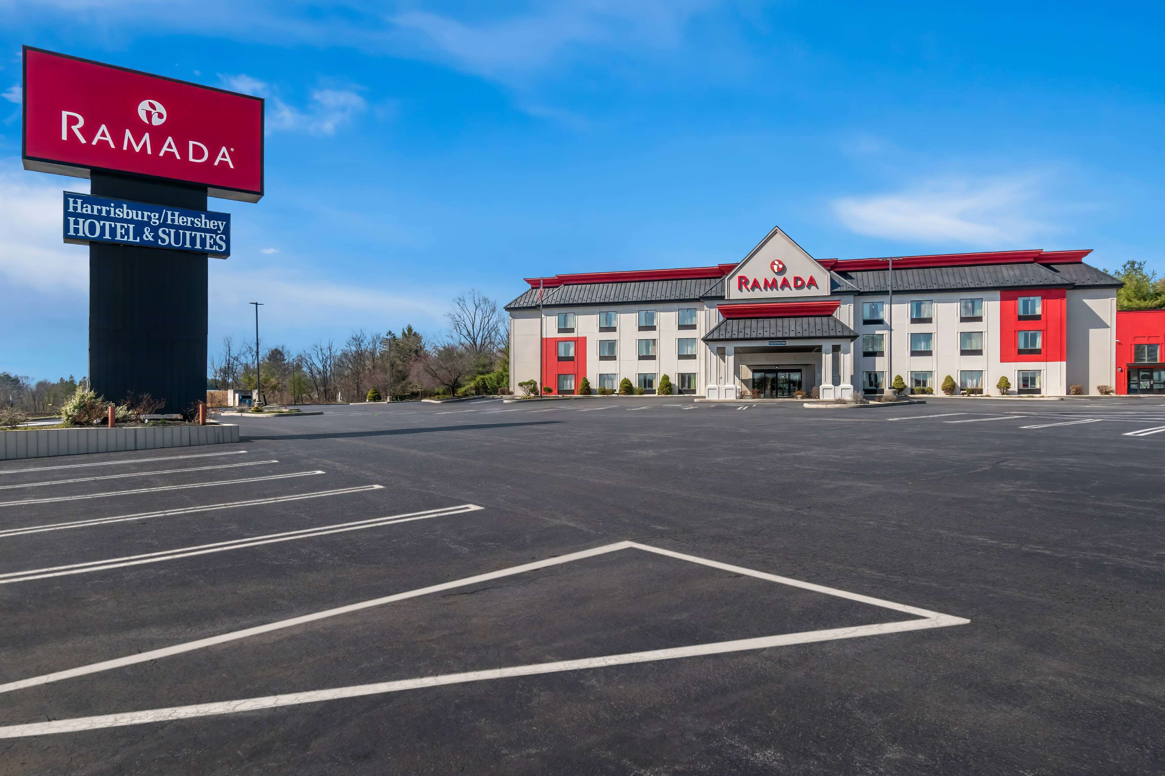 A Ramada Harrisburg/Hershey Hotel & Suites with a large parking lot and a clear blue sky.