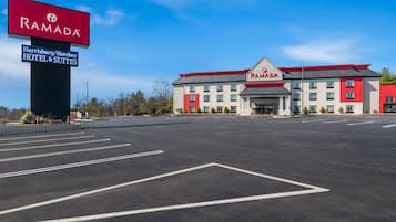 A Ramada Harrisburg/Hershey Hotel & Suites with a large parking lot and a clear blue sky.