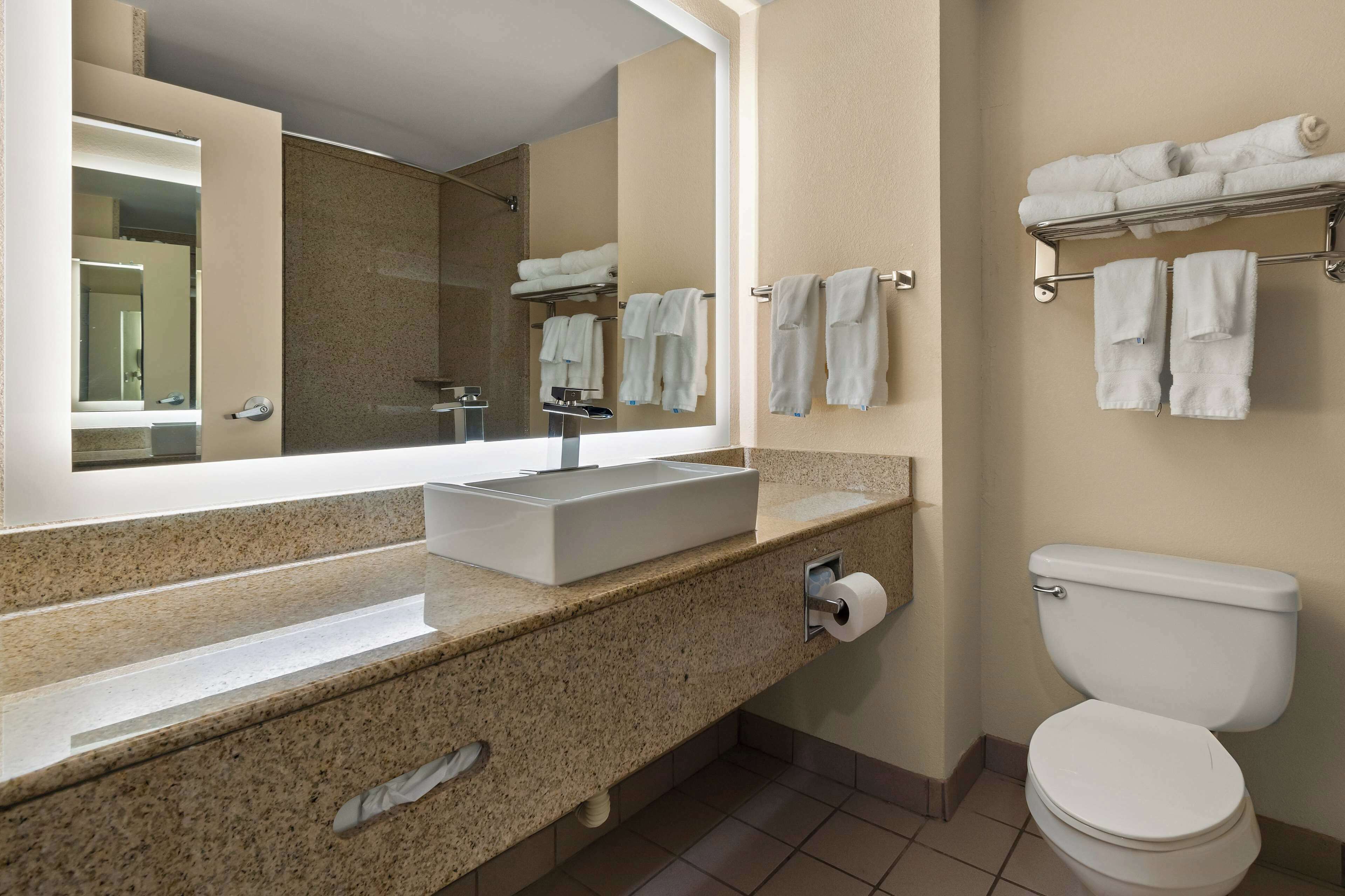 A modern bathroom with a large mirror, a sink, a toilet, and a towel rack.