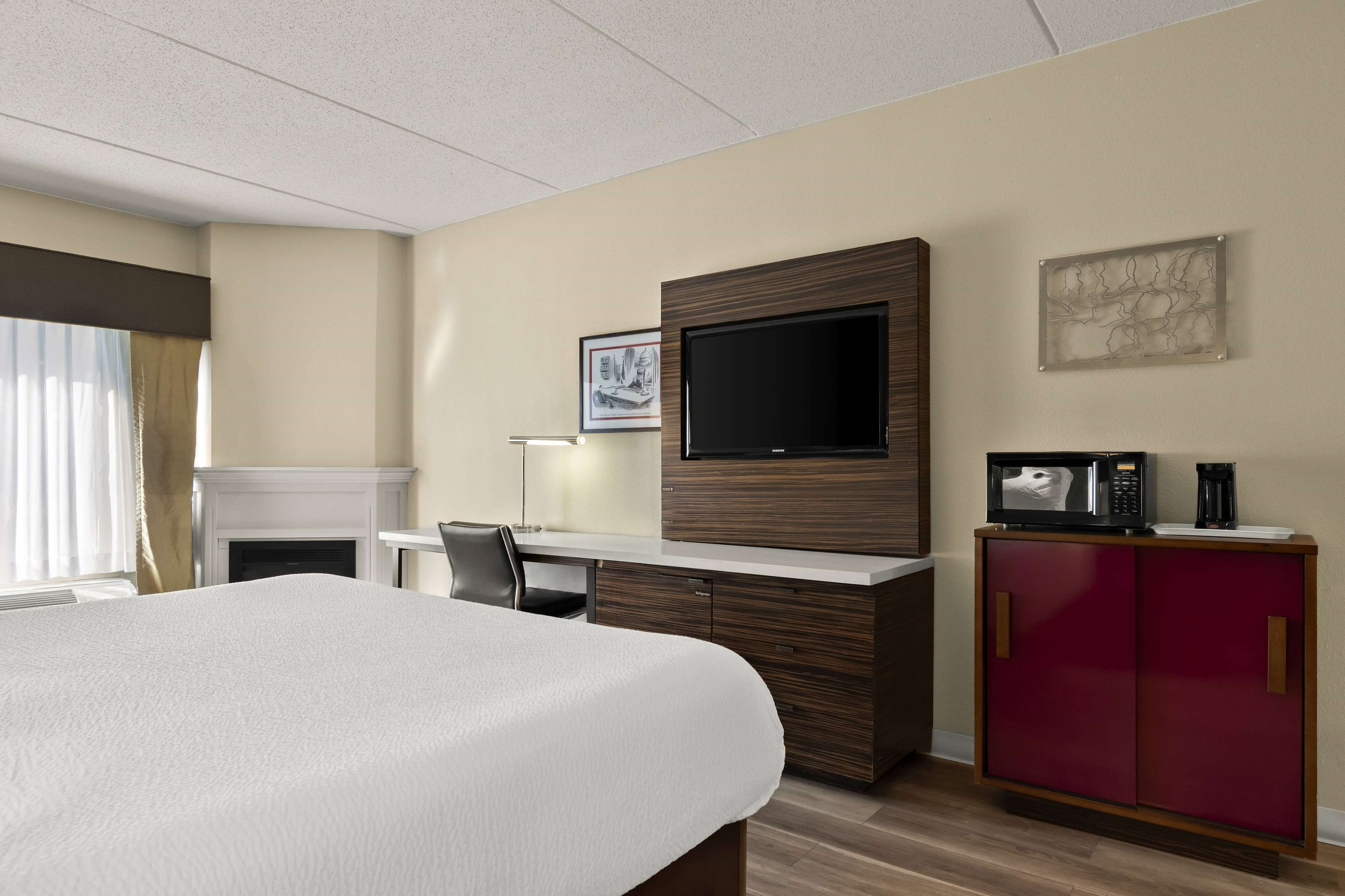 A hotel room with a bed, a desk, a television, a microwave, and a cabinet.