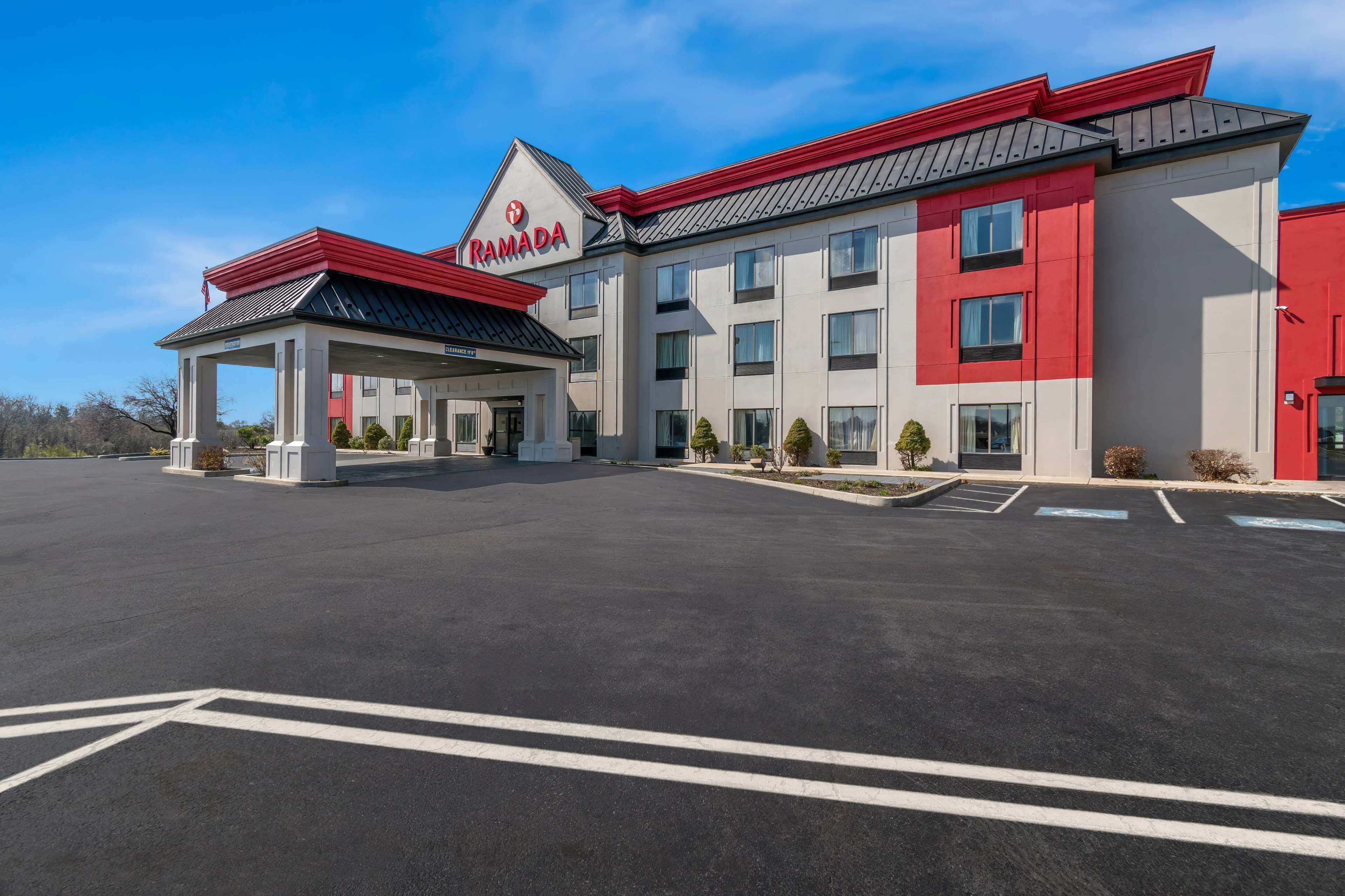 A modern hotel with a red and white facade, a covered entrance, and a parking lot.