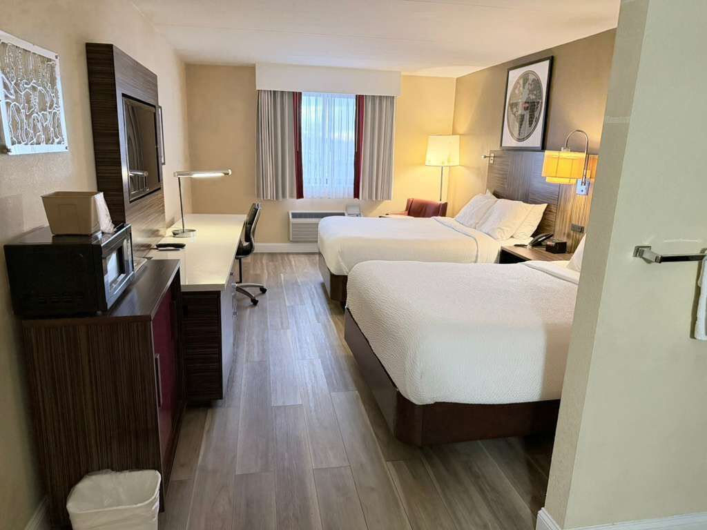 A hotel room with two beds, a desk, a TV, and a window with curtains.