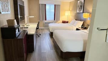 A hotel room with two beds, a desk, a TV, and a window with curtains.