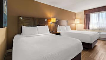 Ein Hotelzimmer mit zwei Betten, einem Holzkopfteil, einem Nachttisch, einer Lampe und einem Fenster mit Vorhängen.