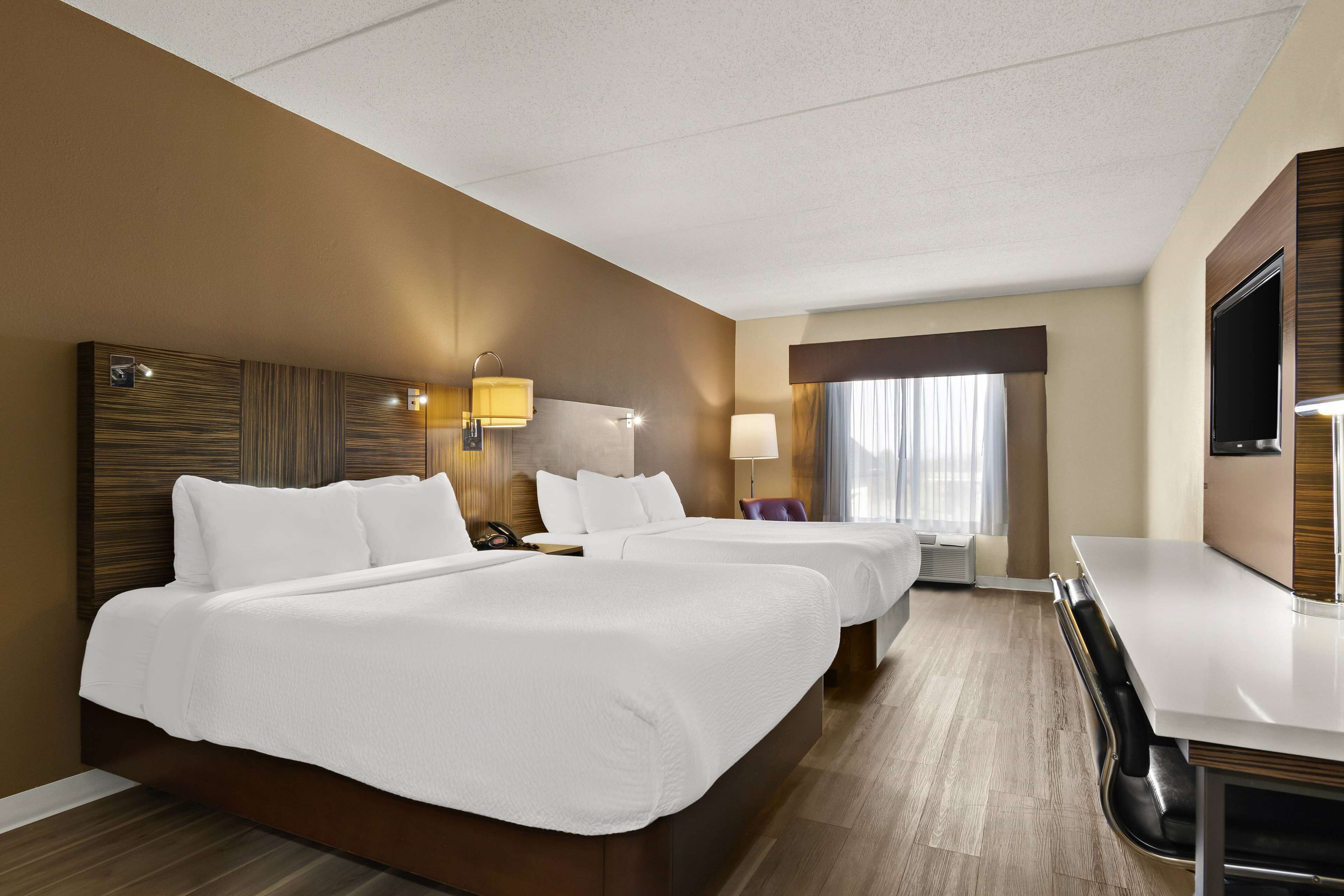 A hotel room with two beds, a desk, a TV, and a window with curtains.