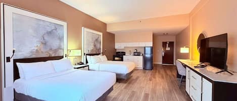 Una habitación de hotel con dos camas, un escritorio, un televisor y una kitchenette.