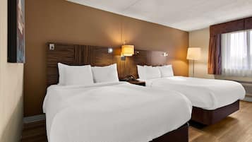 A hotel room with two beds, a wooden headboard, a nightstand, a lamp, and a window with curtains.