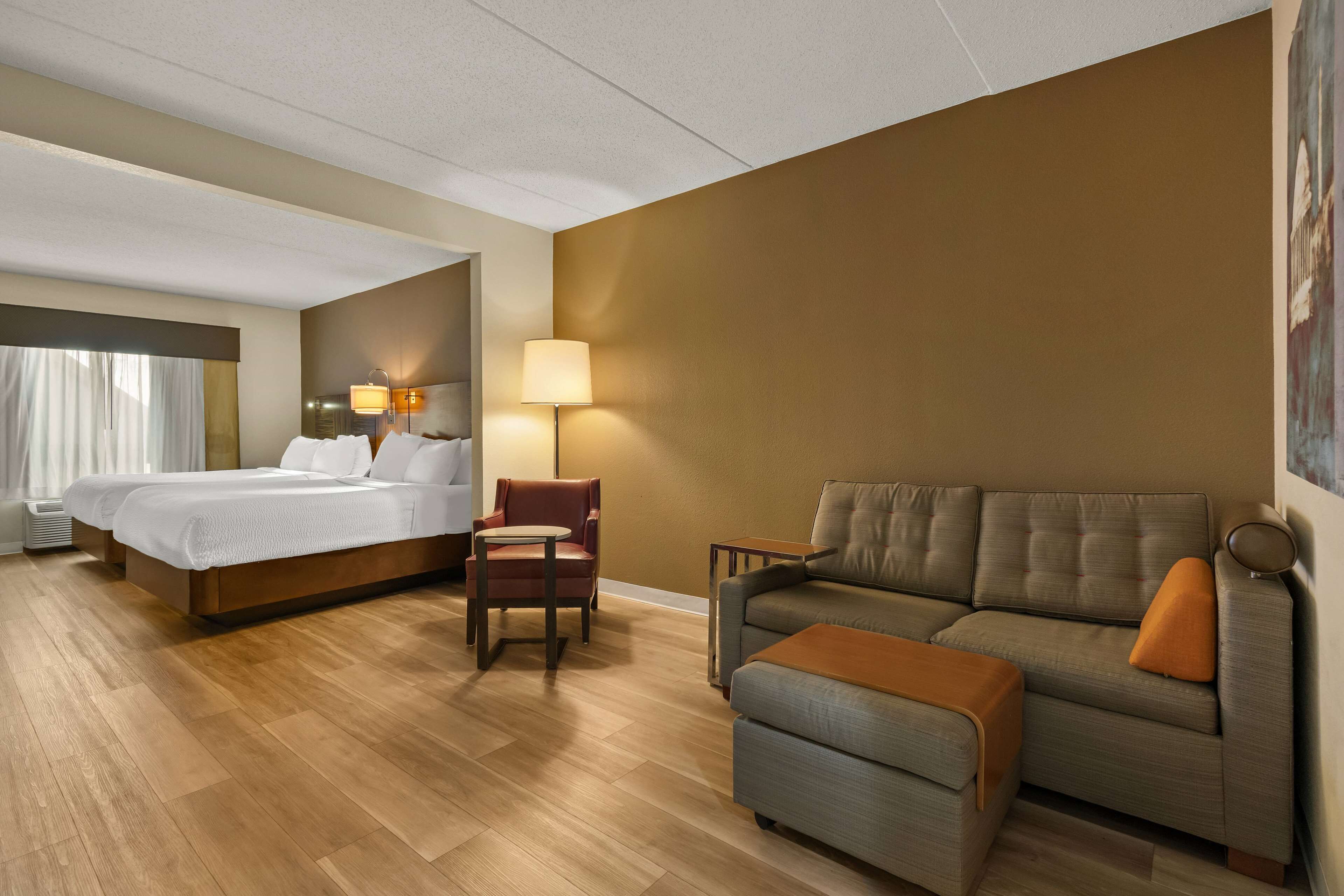Una habitación de hotel con cama, sofá, sillón, mesita y lámpara.