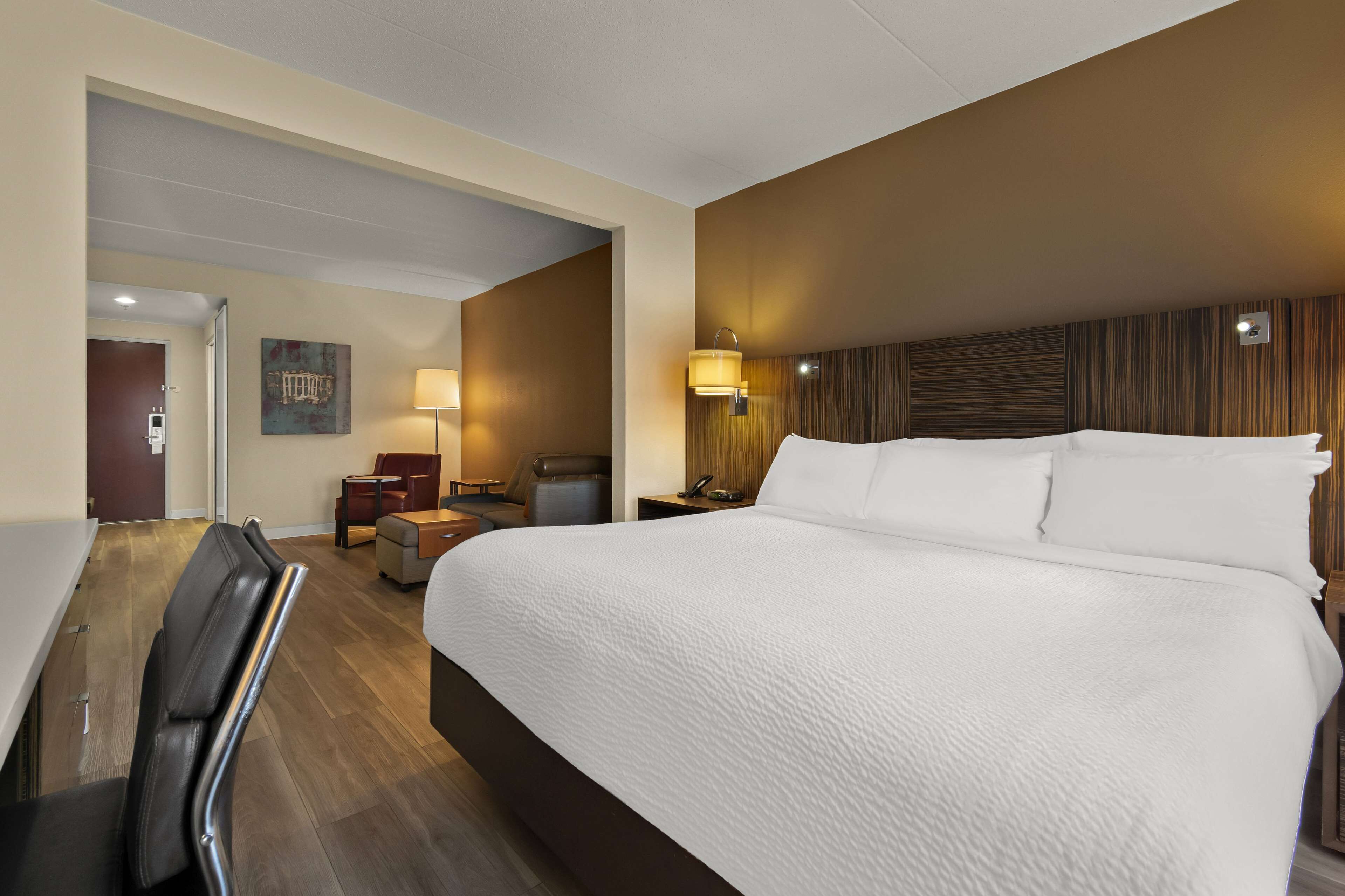 A hotel room with a large bed, a desk, a chair, a lamp, and a painting on the wall.