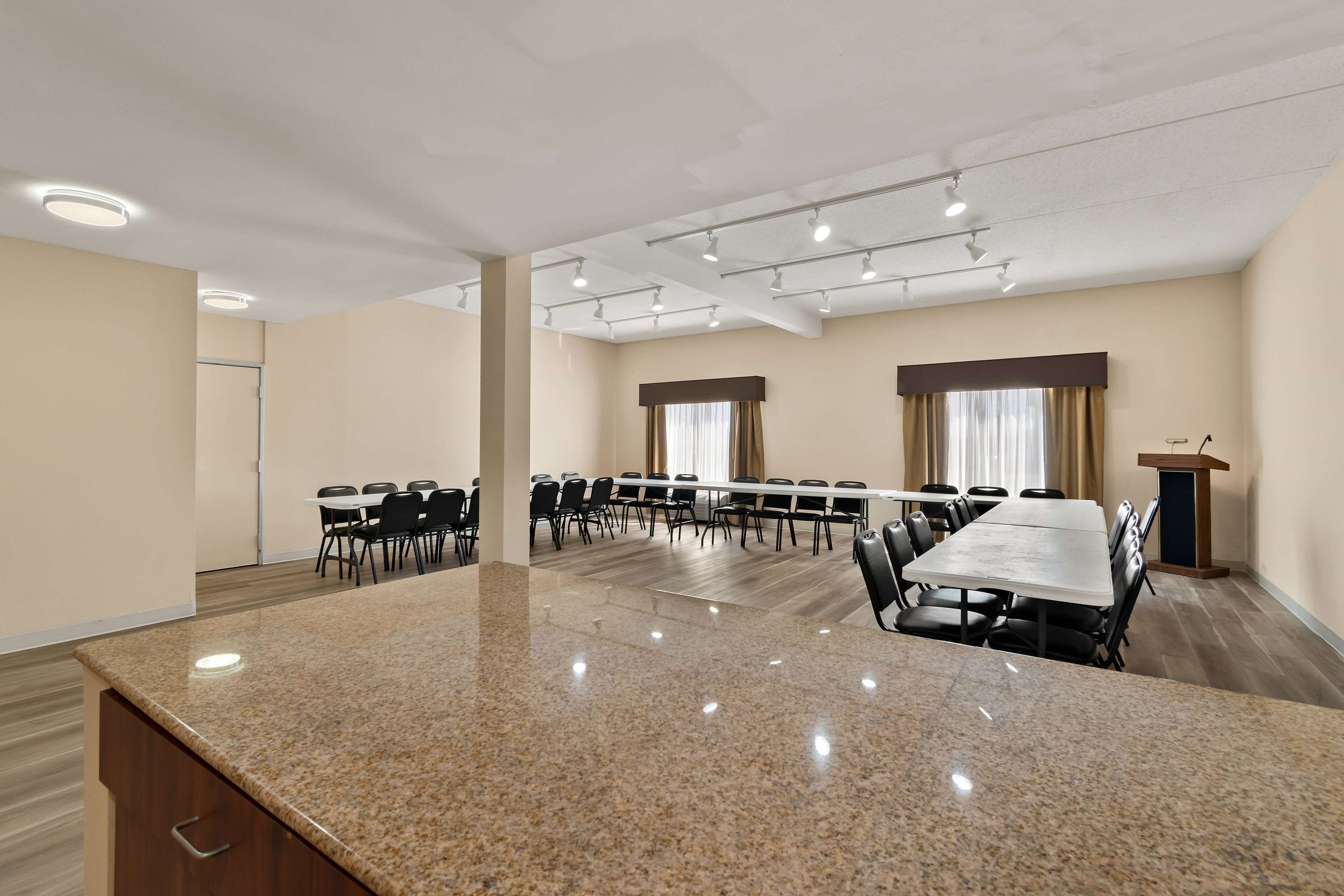 A conference room with a large granite table, multiple chairs, a podium, and a window with curtains.