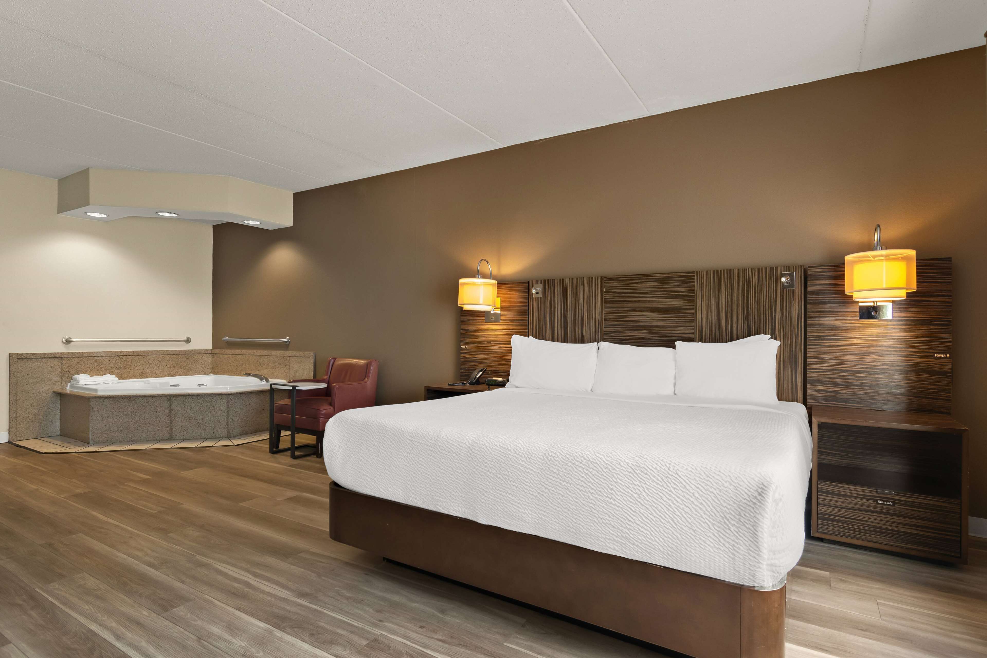 A modern hotel room with a large bed, a separate seating area, a built-in bathtub, and two wall-mounted lamps.