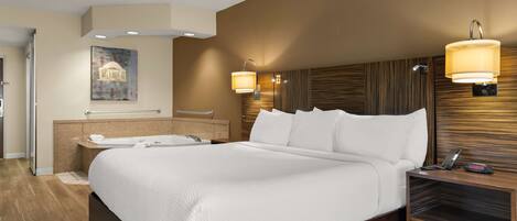 A hotel room with a large bed, a built-in bathtub, a vanity with a mirror, and two wall-mounted lamps.