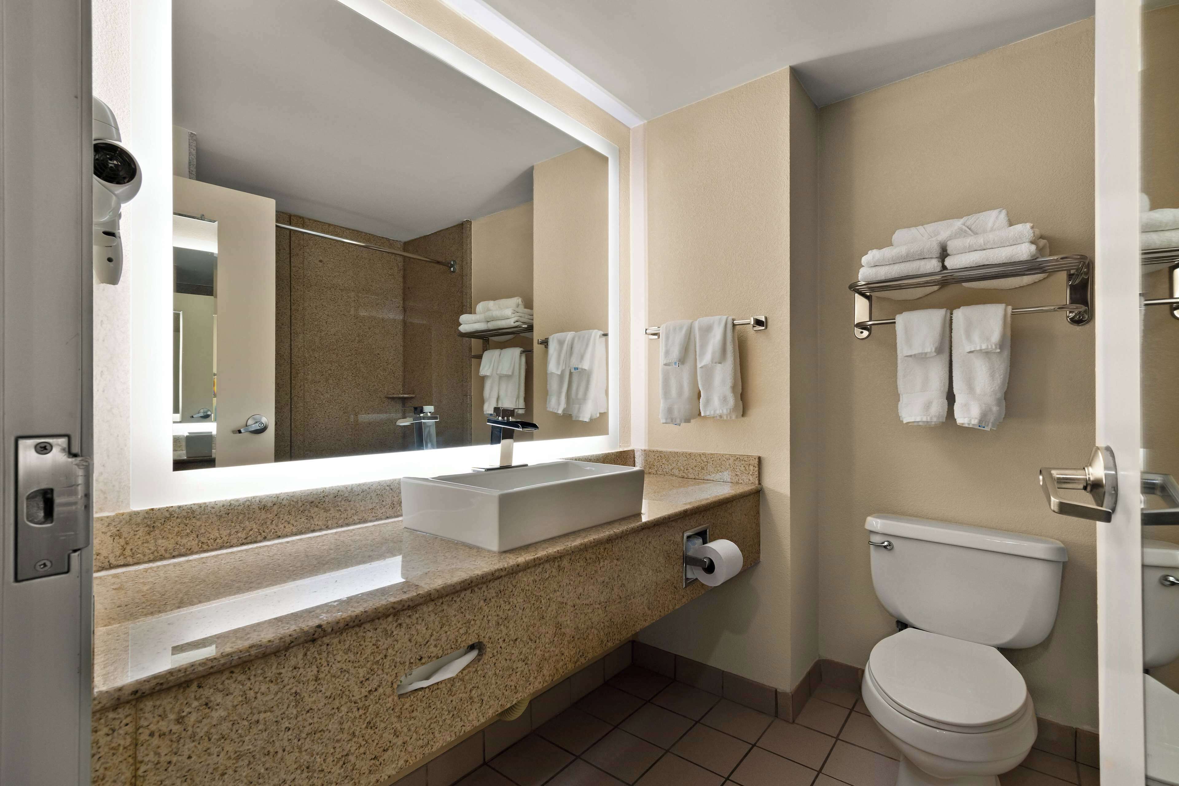 A modern bathroom with a large mirror, a sink, a toilet, and towel racks.