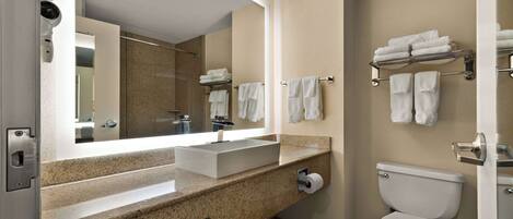 A modern bathroom with a large mirror, a sink, a toilet, and towel racks.