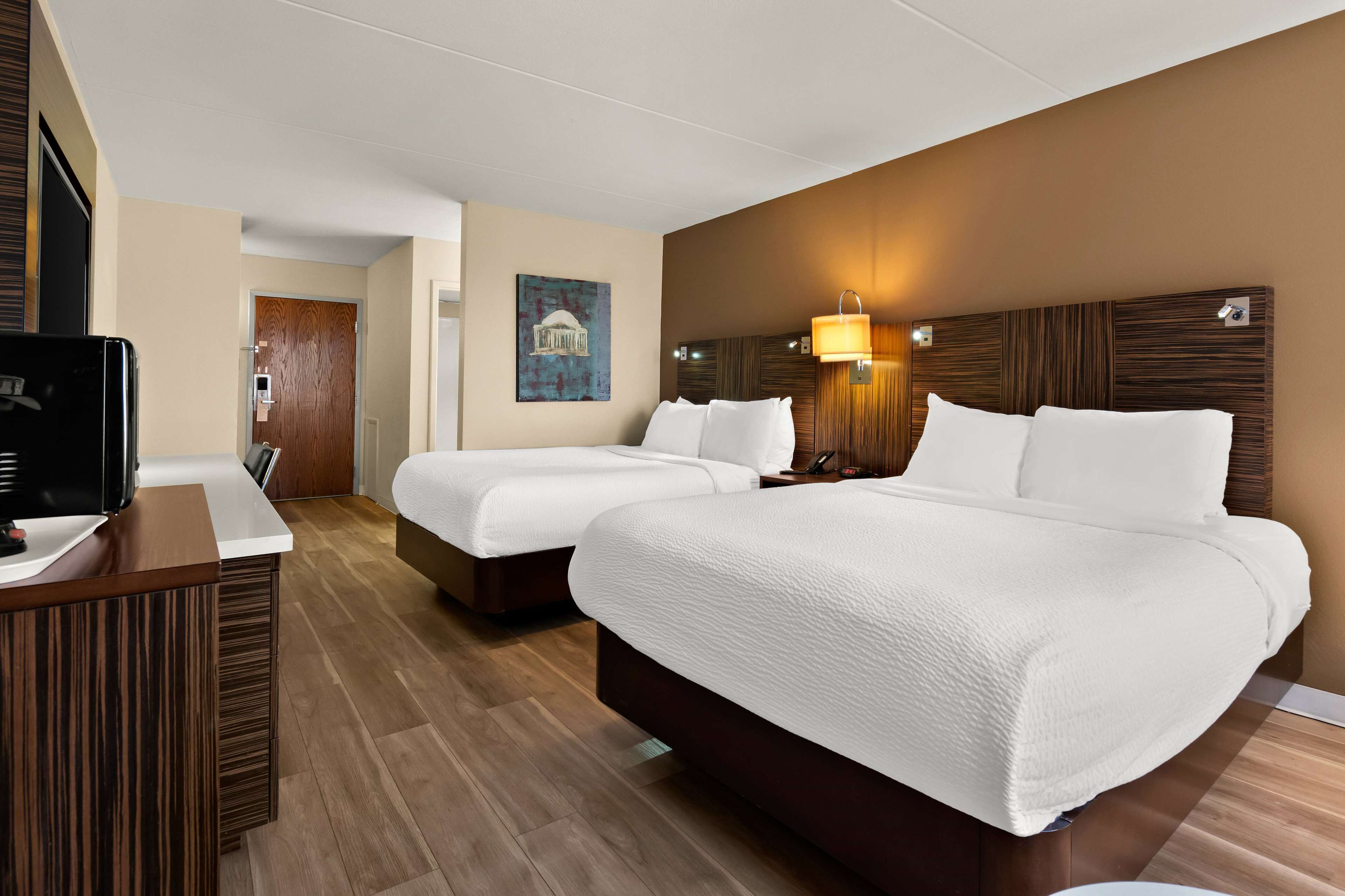 Ein Hotelzimmer mit zwei Betten, einem Schreibtisch, einem Fernseher und einer Wandleuchte.