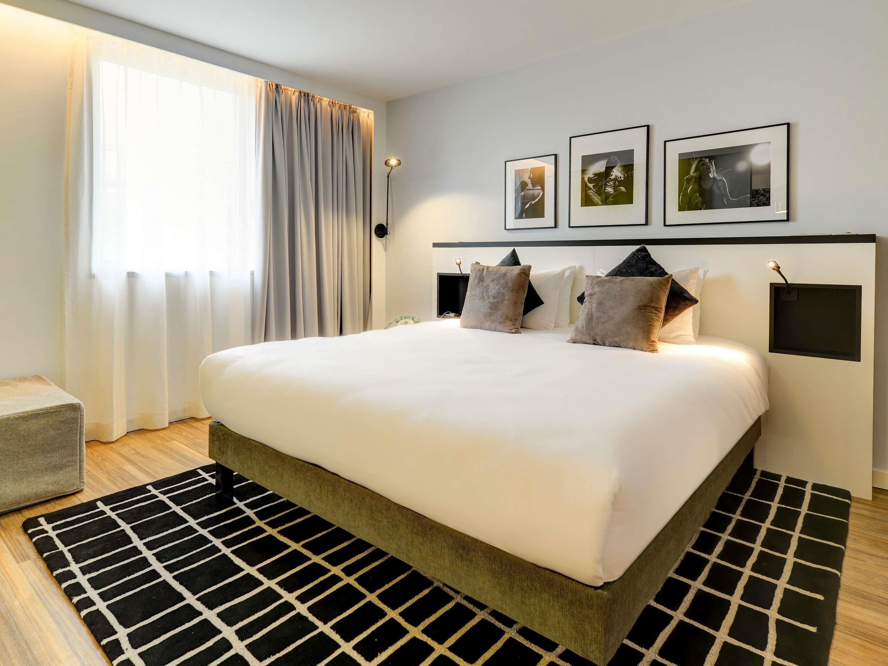 Una habitación de hotel moderna con una cama grande, una mesita de noche, una lámpara y tres cuadros en la pared.