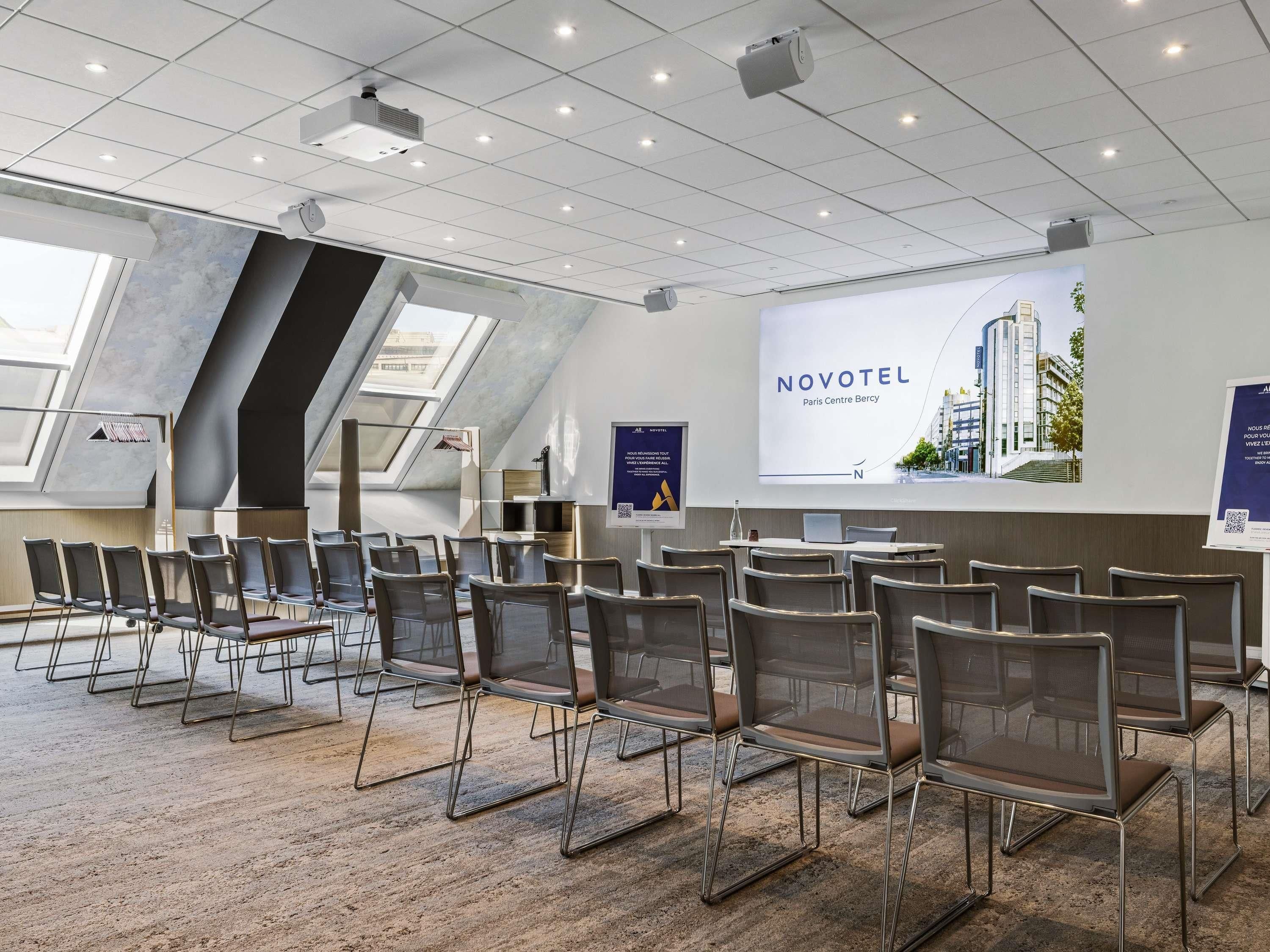 A conference room with rows of chairs, a projector screen, and a large window with a view of the city.