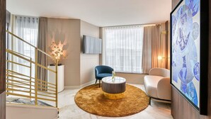 A modern living room with a staircase, a round coffee table, two chairs, a TV, and a large abstract painting. - Novotel Paris Centre Bercy (Paris)