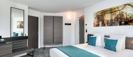 A modern hotel room with a large bed, a desk, and a wardrobe.