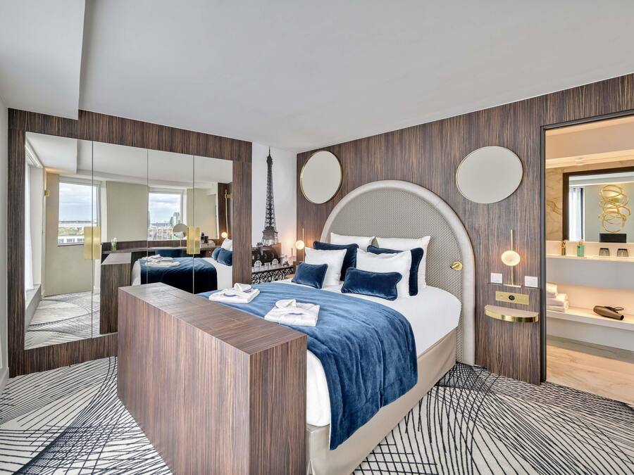 A modern hotel room with a large bed, a wooden console table, a mirror, and a view of the Eiffel Tower.
