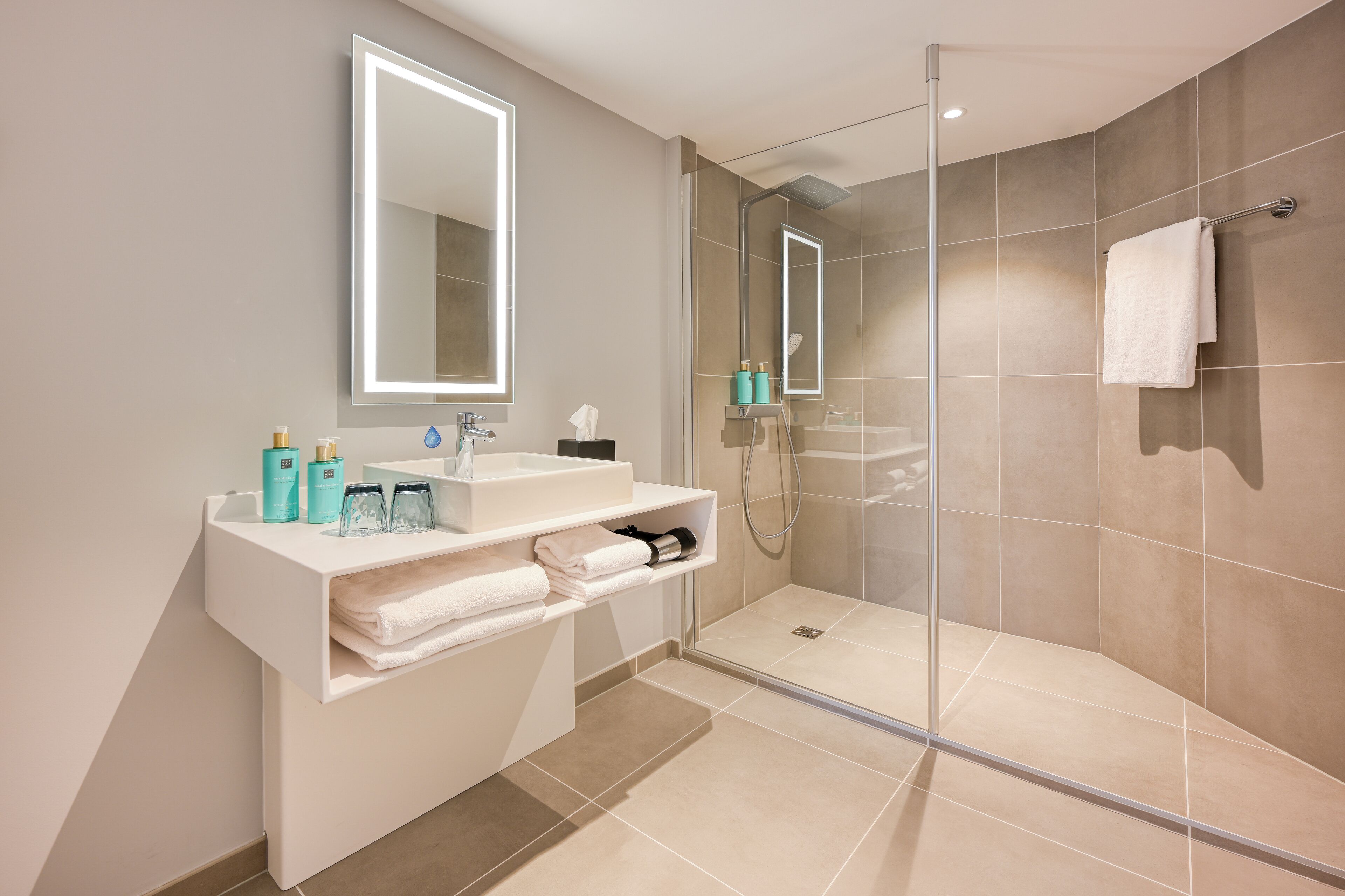 A modern bathroom with a glass-enclosed shower, a white vanity with a mirror, and neatly arranged toiletries.