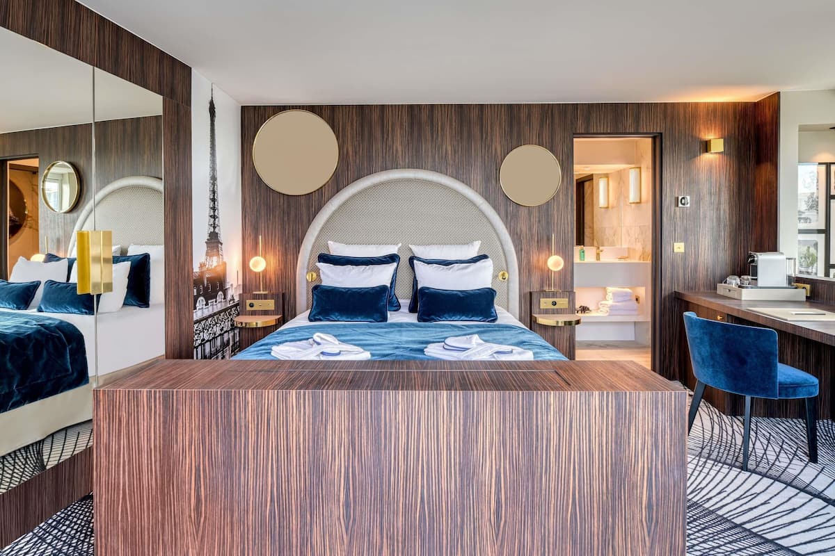 A modern hotel room with a large bed, a desk, and a bathroom visible through an open door.
