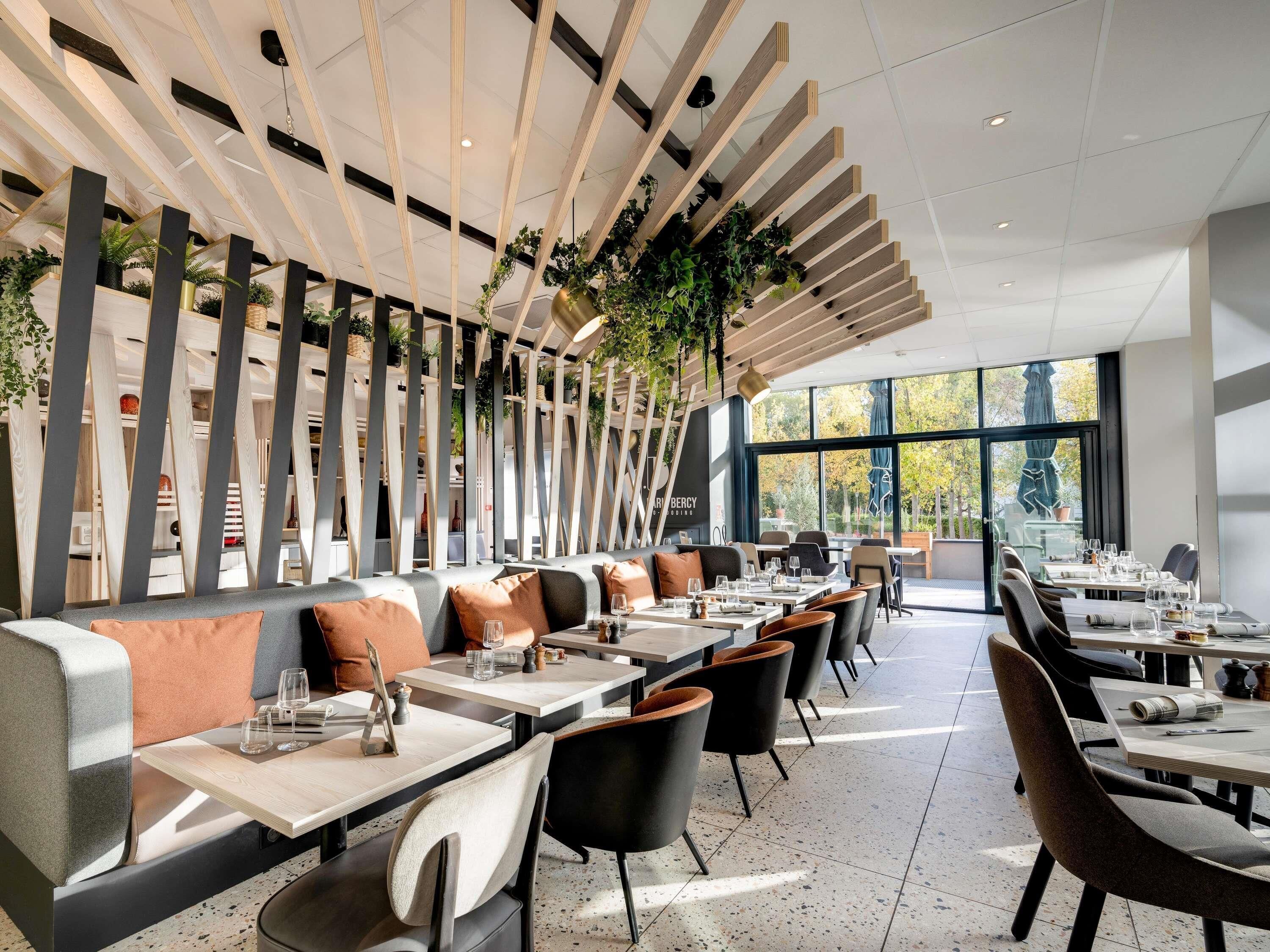 Interior de restaurante moderno con techos altos, listones de madera y ventanas amplias.