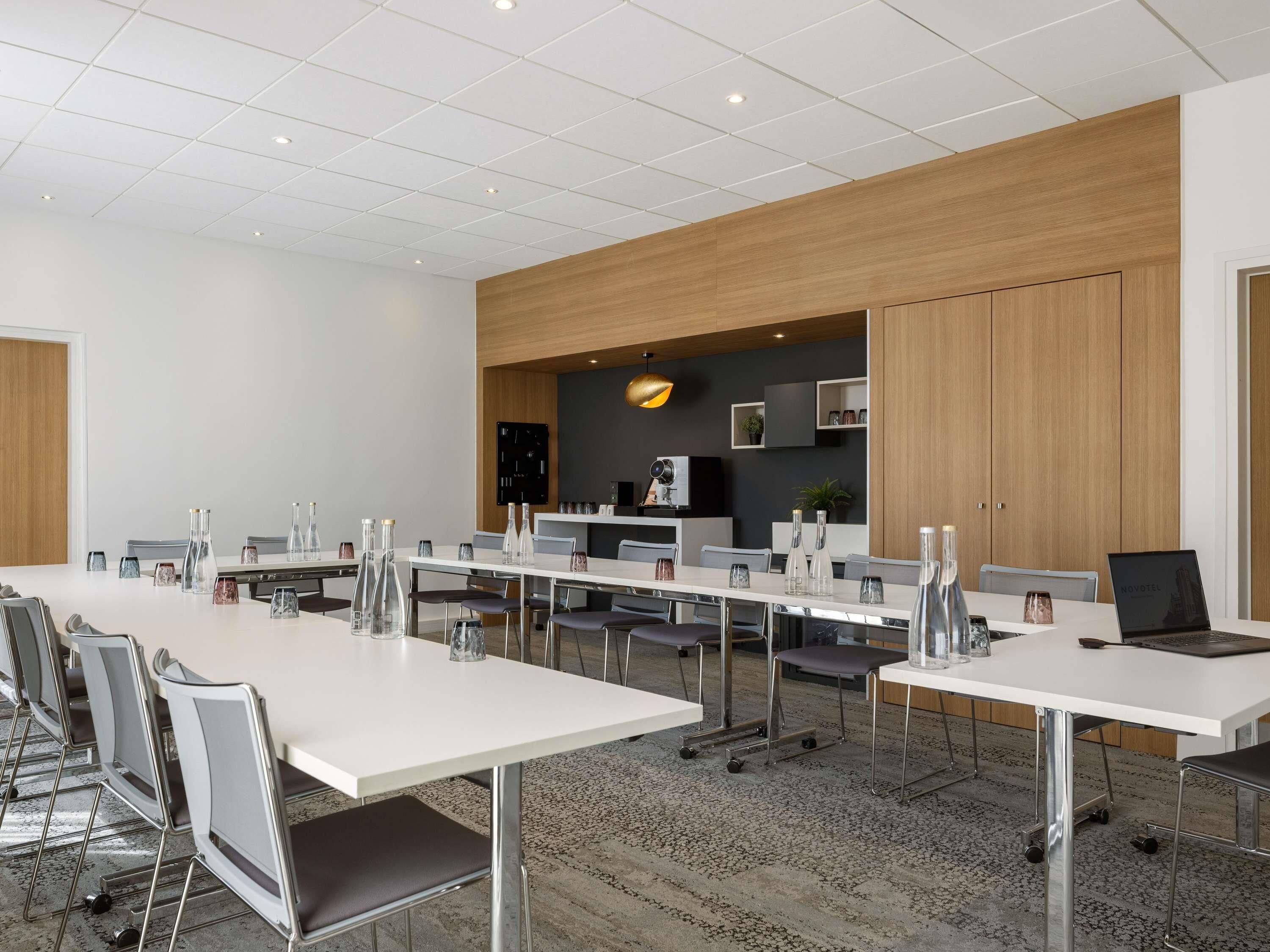 Un salón de conferencias moderno con mesas blancas, sillas grises y una pared de acento de madera.