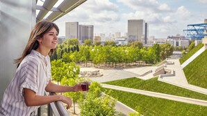 A person holding a glass of red drink, overlooking a cityscape with modern buildings and green spaces. - Novotel Paris Centre Bercy (Paris)