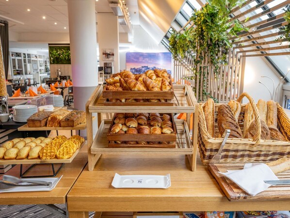 A bakery display with various pastries and bread, including croissants and baguettes, in a modern setting with a view of the cityscape. - Novotel Paris Centre Bercy (Paris)