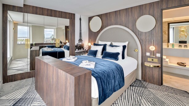 A modern hotel room with a large bed, a wooden desk, a mirror, and a view of the Eiffel Tower. - Novotel Paris Centre Bercy (Paris)