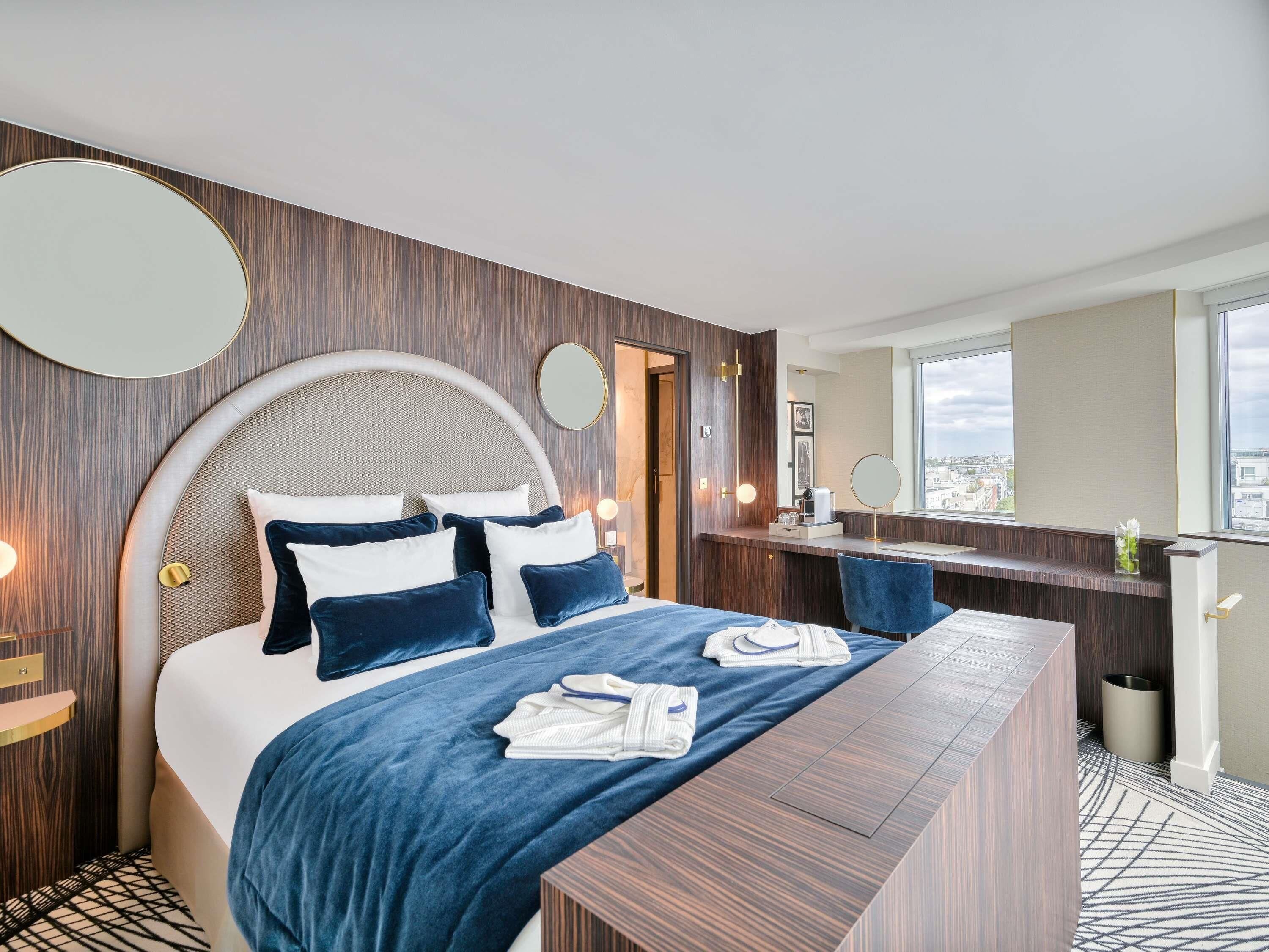 A modern hotel room with a large bed, a desk, and a view of the city.