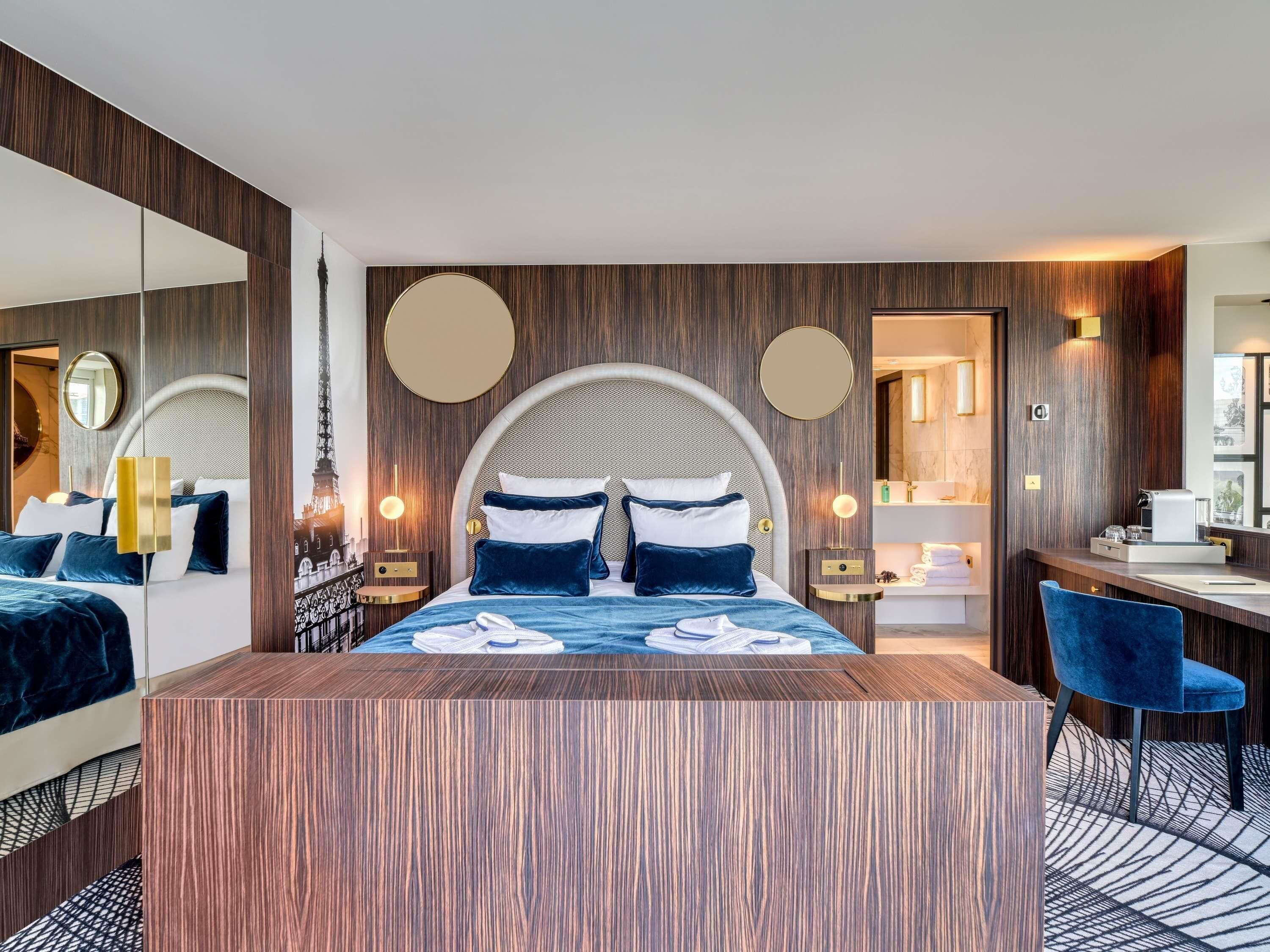 Une chambre d’hôtel moderne, dotée d’un grand lit, de tables de chevet, d’un bureau et d’une salle de bain visible à travers une porte ouverte.