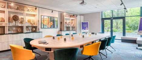 A conference room with a round table, chairs, a projector, and decorative items on shelves.
