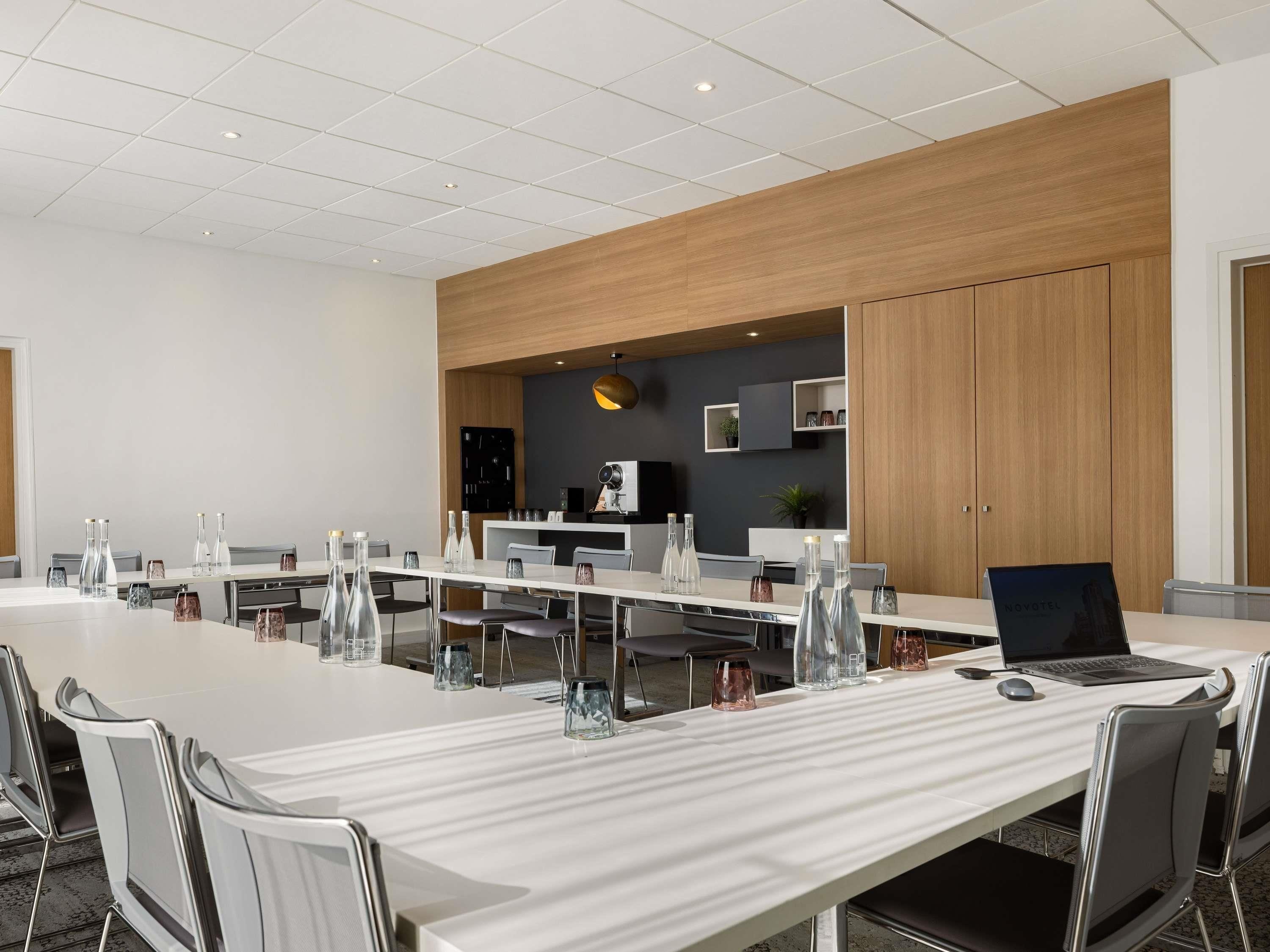 A modern conference room with a long table, multiple chairs, and a laptop on the table.