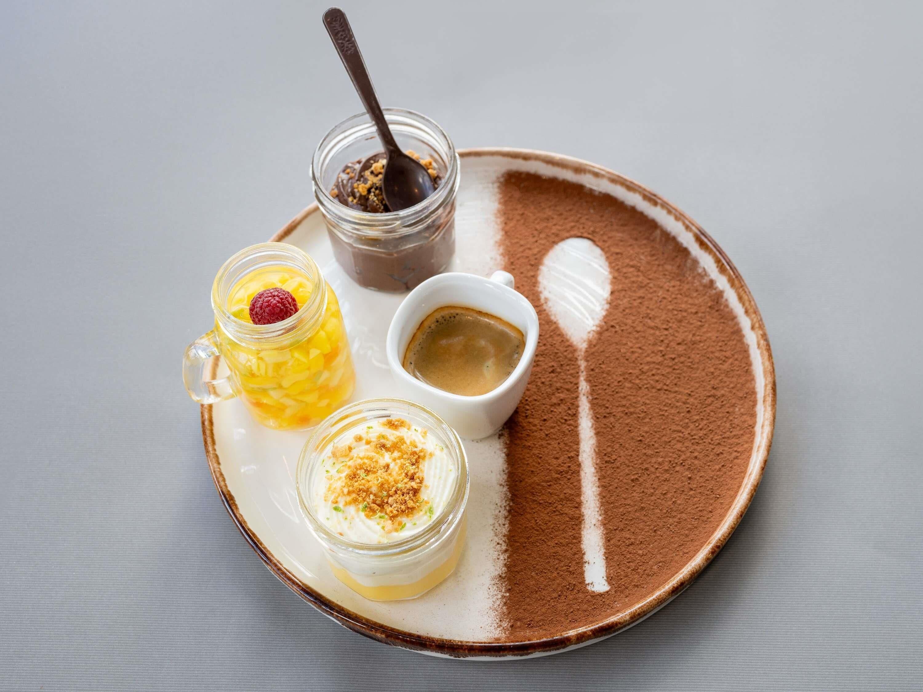 A dessert tray with a coffee cup, a jar of chocolate spread, and a jar of fruit compote.