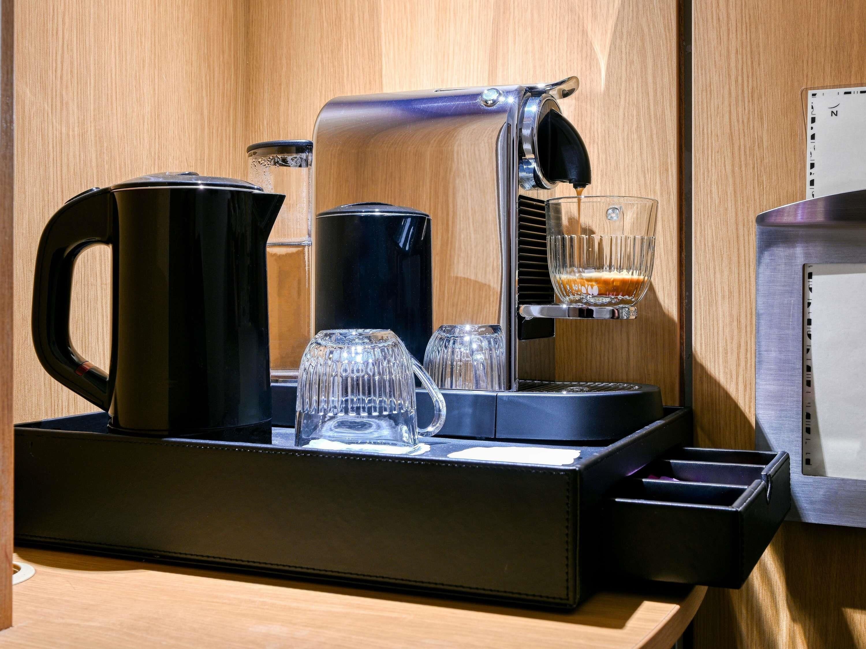 A coffee machine with a glass carafe, a coffee pot, and a glass on a tray.