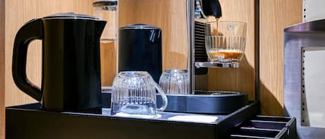 A coffee machine with a glass carafe, a coffee pot, and a glass on a tray.