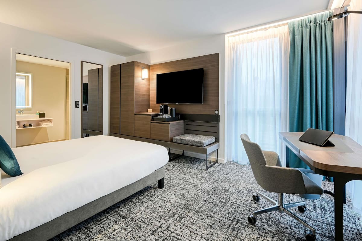 A hotel room with a bed, a desk with a laptop, a TV, and a seating area with chairs.