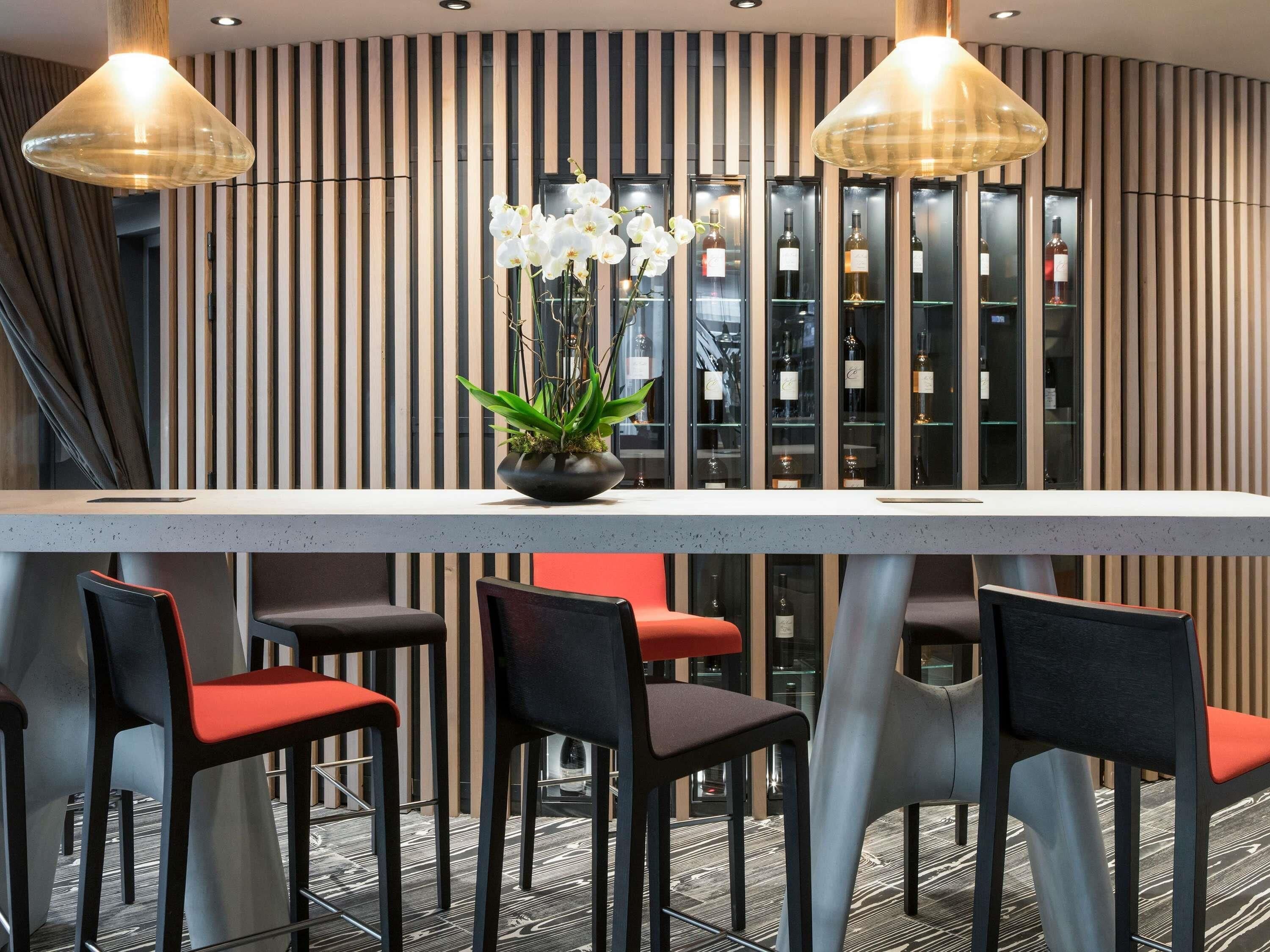 Un espace bar moderne avec un long comptoir, de nombreux tabourets et une plante en pot.
